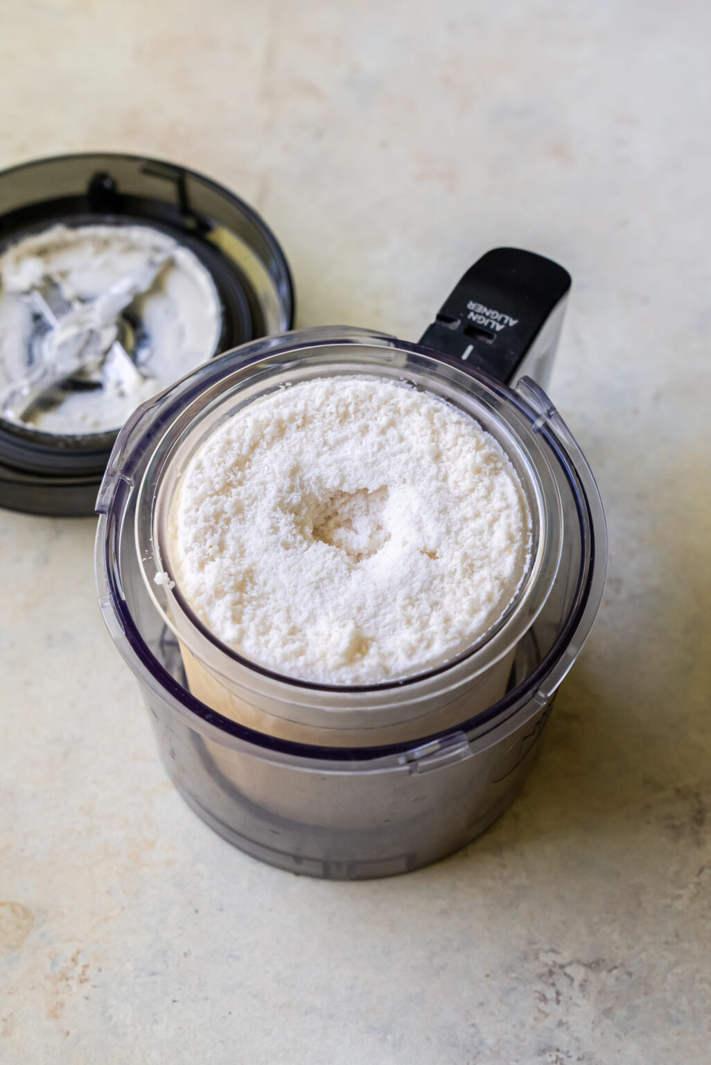 A food processor container filled with powdered ingredients sits on a countertop, with its lid placed beside it, ready to create a delicious Strawberry Cheesecake-flavored Ninja Creami treat.