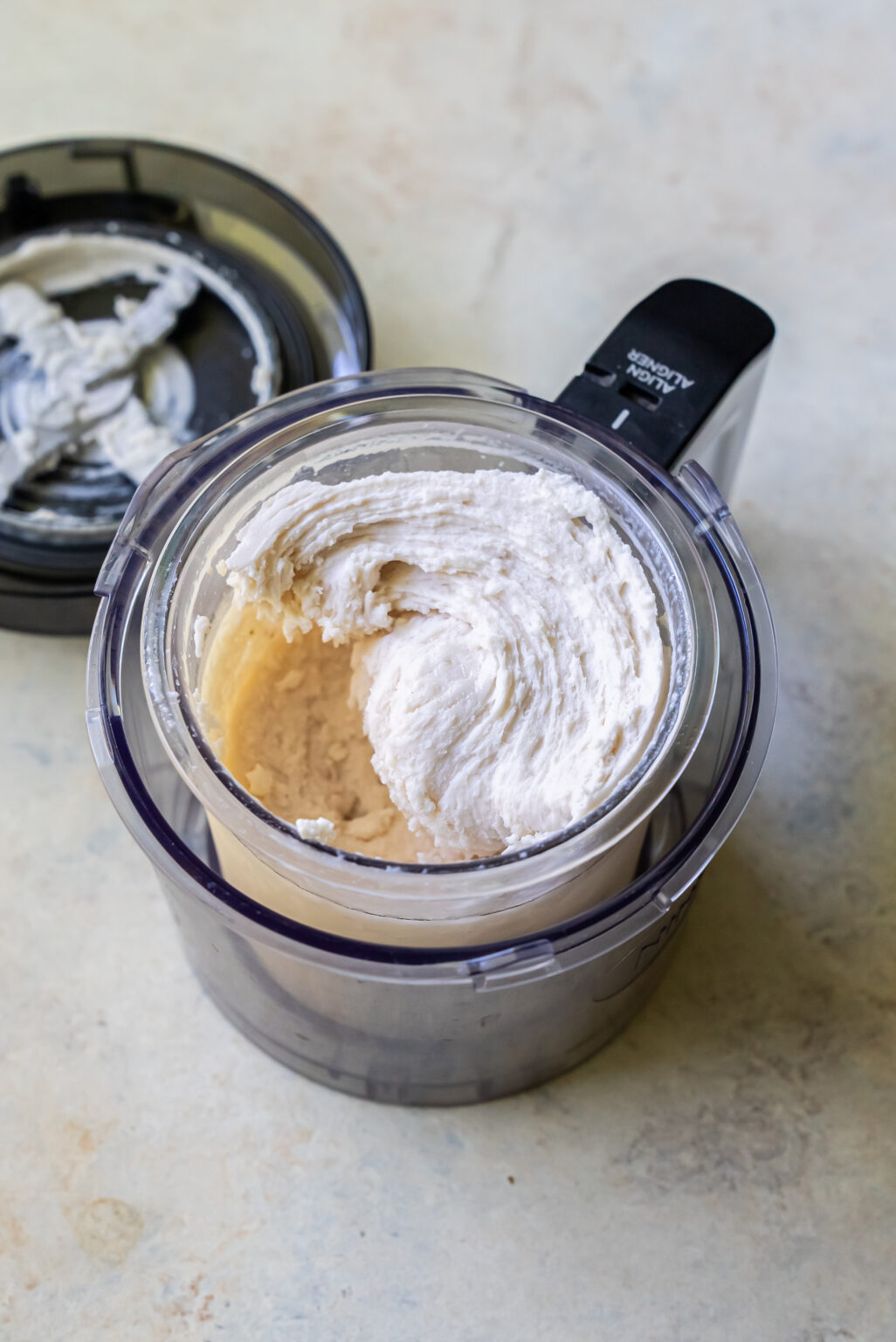 A food processor containing a smooth, freshly made Strawberry Cheesecake whipped mixture with its lid placed beside it.