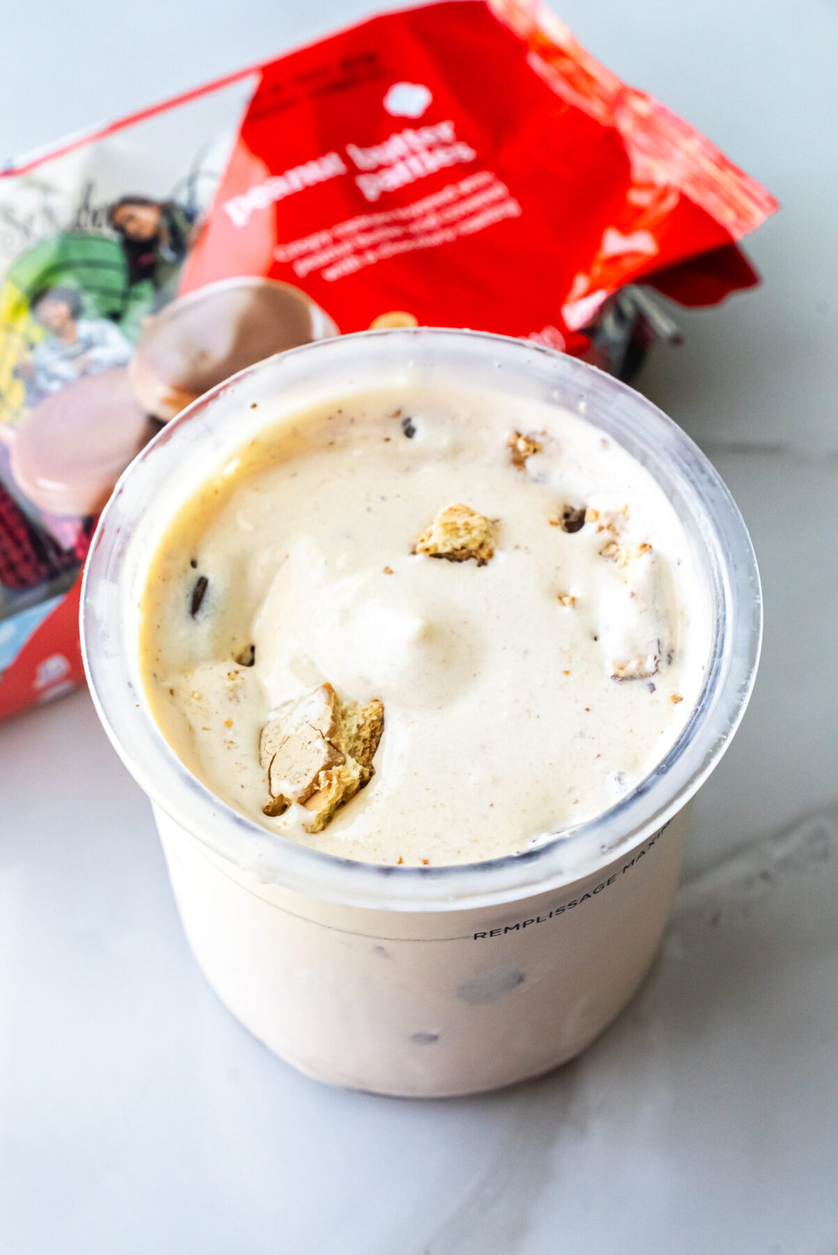 Overhead shot of Peanut Butter Patties Ninja Creami Ice Cream in a clear pint. Broken cookie pieces are mixed into the white base. The red cookie packaging sits behind the pint.