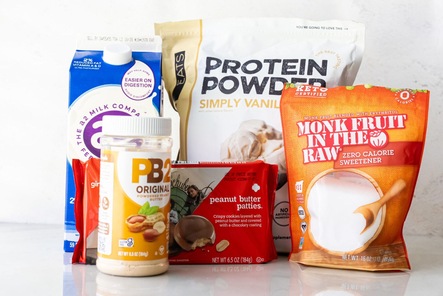 Flat lay of ingredients for Peanut Butter Patties Ninja Creami Ice Cream: a2 milk, PB2 powdered peanut butter, Simply Vanilla protein powder, Girl Scout Peanut Butter Patties, and Monk Fruit in the Raw sweetener.