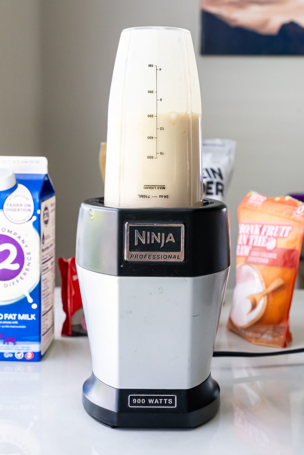 Ninja Professional blender filled with beige liquid base for Peanut Butter Patties Ninja Creami Ice Cream. Ingredient packages including a2 milk and Monk Fruit sweetener are arranged on the counter around the blender.