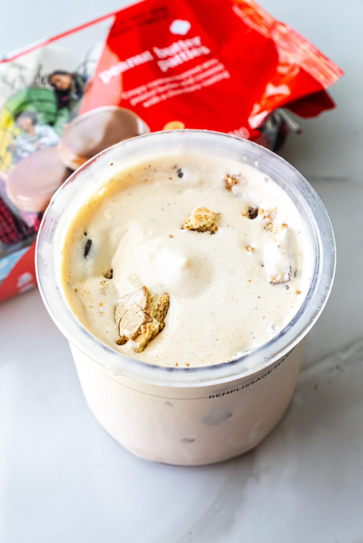 Slightly angled view of Peanut Butter Patties Ninja Creami Ice Cream in a pint. Cookie chunks are visible in the creamy base. The red cookie packaging is blurred in the background.