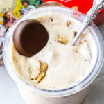 Top-down view of Peanut Butter Patties Ninja Creami Ice Cream in a clear pint. A whole chocolate-covered cookie sits on top alongside broken pieces, with an ornate silver spoon inserted into the mixture.