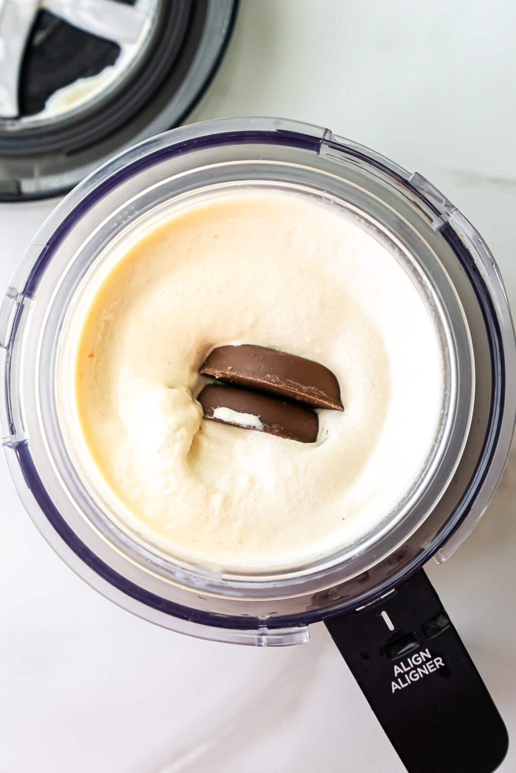 Overhead shot of broken Peanut Butter Patties cookies placed into the center well of spun ice cream in a Ninja Creami pint, ready for the mix-in cycle to incorporate cookie pieces.