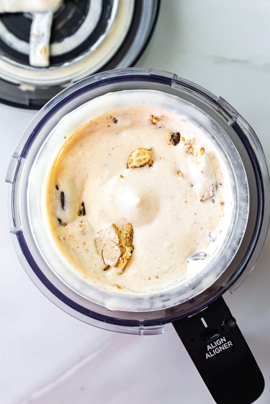 Close-up of finished Peanut Butter Patties Ninja Creami Ice Cream in a pint with an ornate silver spoon inserted. Broken cookie pieces are visible throughout the creamy white base.