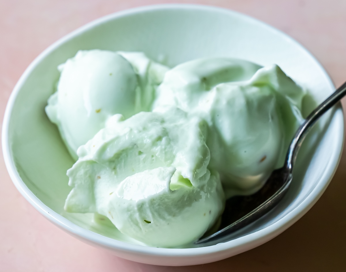 A white bowl filled with scoops of light green ice cream, made using the Ninja Creami, with a metal spoon resting inside the bowl.