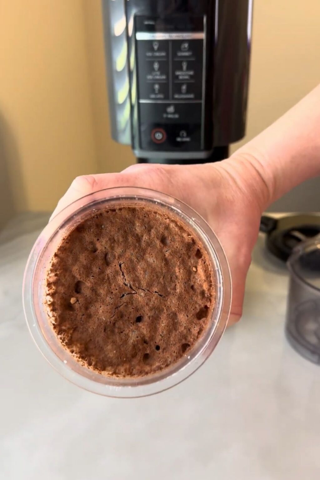 Hand holding a frozen Ninja Creami pint showing cracked, solidified chocolate-mint base surface.