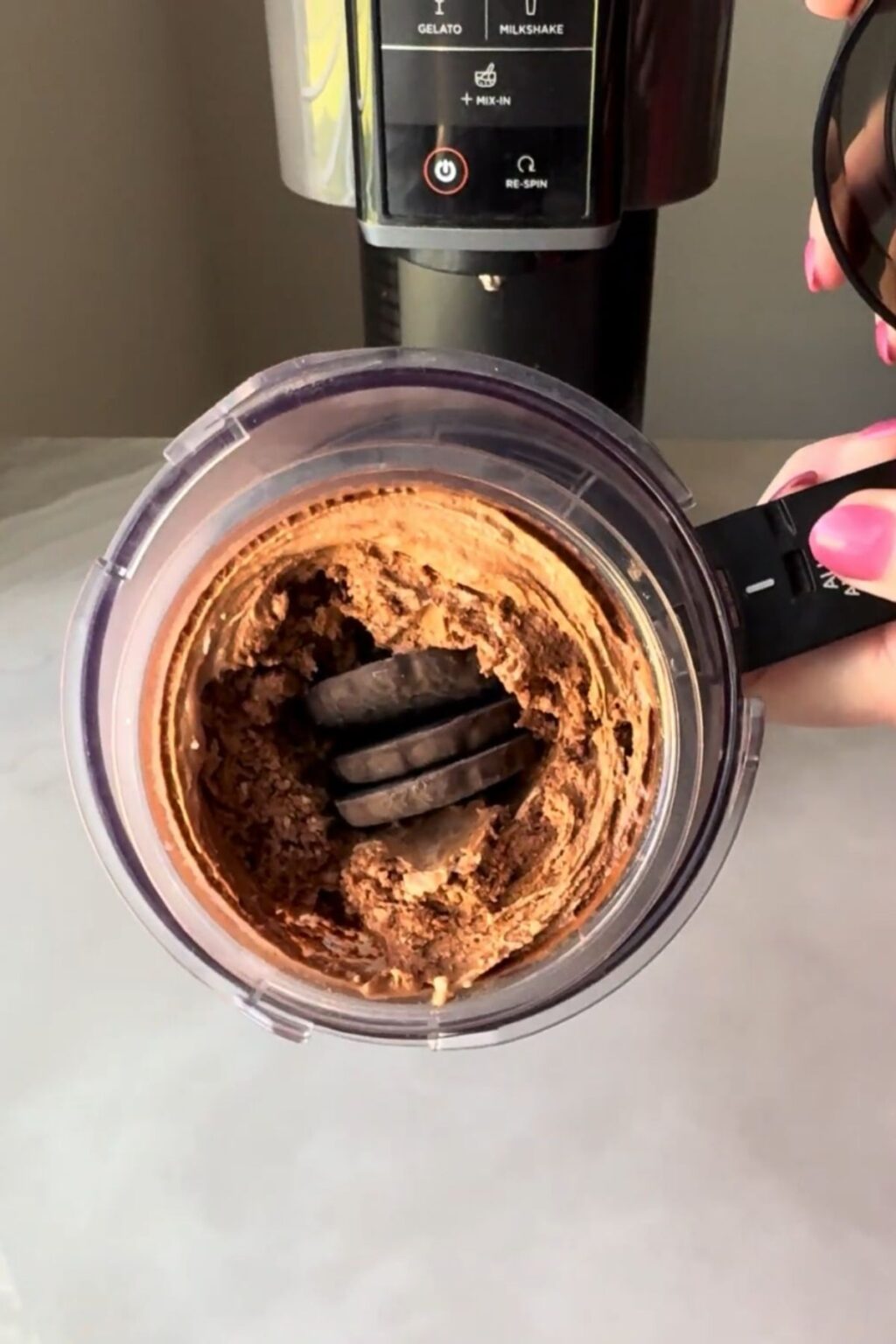 Hand placing whole Girl Scouts Thin Mints cookies into the center of spun chocolate ice cream inside the Ninja Creami pint, preparing for final “Mix-In” cycle to create authentic mint-chocolate crunch.